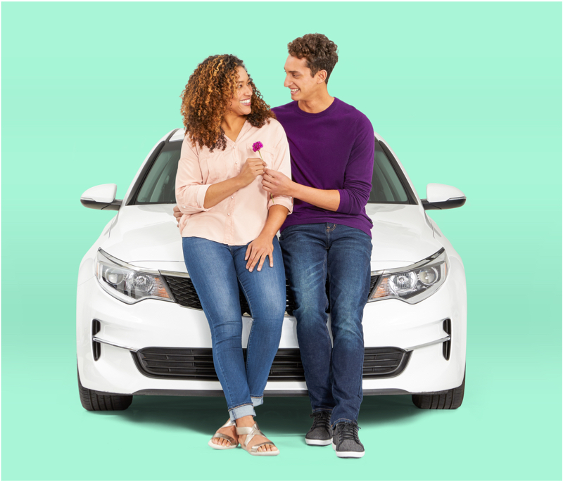 man and woman holding a flower, sitting against the front of a car